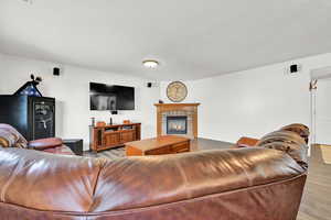 Living room with a textured ceiling, wood-type flooring, and a brick fireplace