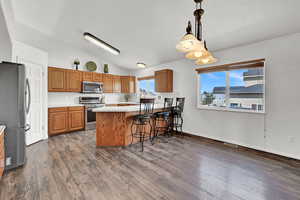 Kitchen with a breakfast bar, dark wood-type flooring, stainless steel appliances, pendant lighting, and vaulted ceiling