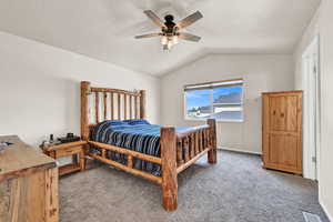 Carpeted bedroom featuring ceiling fan and vaulted ceiling