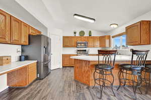 Kitchen with lofted ceiling, dark hardwood / wood-style floors, stainless steel appliances, and a kitchen bar