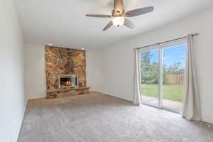 Second view of casual living room featuring carpet floors, a fireplace, and ceiling fan sliding glass doors walking out to the backyard.