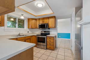 Kitchen with light tile flooring, sink, stainless steel appliances, a raised ceiling and a new window with farmhouse-style trim.