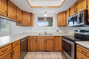 Kitchen with light tile flooring, sink, stainless steel appliances, a raised ceiling and a new window with farmhouse-style trim.