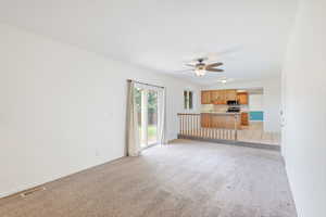 Casual living room with light carpet, a ceiling fan and sliding glass doors walking out to the backyard.