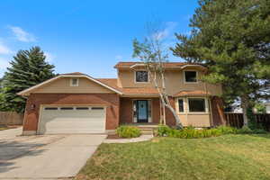 View of front of property featuring a garage, a front lawn, and mature trees.