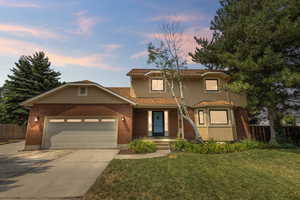 Twilight view of front facade with a garage, a yard and mature trees.