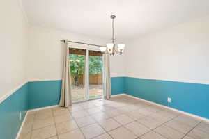 Tiled formal dining area with ornamental molding, a chandelier and sliding doors walking out to the backyard.