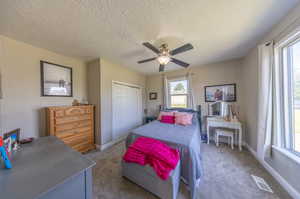 Bedroom with a textured ceiling, carpet, a closet, and ceiling fan