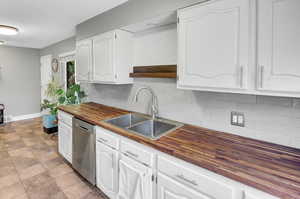 Kitchen featuring wooden counters, sink, stainless steel dishwasher, decorative backsplash, and white cabinetry