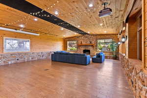 Entertainment room with wood walls, wooden ceiling, a stone fireplace, and hardwood / wood-style floors