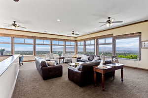 Carpeted living room featuring crown molding, ceiling fan, and a healthy amount of sunlight