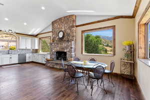 Dining room with vaulted ceiling, a stone fireplace, sink, crown molding, and dark hardwood / wood-style floors