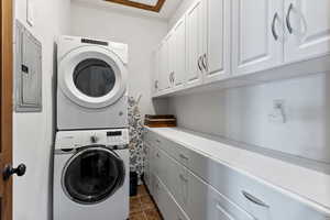 Washroom with cabinets, dark tile patterned flooring, and stacked washer and dryer