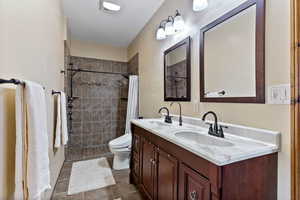 Bathroom with toilet, tile patterned floors, a shower with curtain, and double vanity