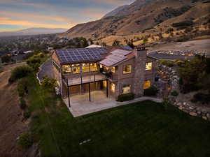 Back house at dusk featuring solar panels, a mountain view, and a lawn