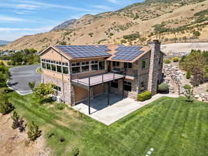 Back of property featuring solar panels, a balcony, a mountain view, and a lawn