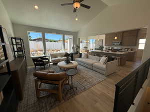 Living room featuring a textured ceiling, high vaulted ceiling, light wood-type flooring, ceiling fan, and sink