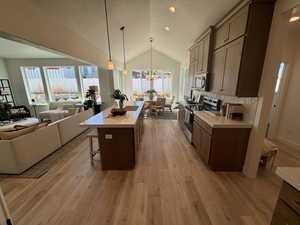 Kitchen featuring appliances with stainless steel finishes, pendant lighting, a center island, and light hardwood / wood-style floors