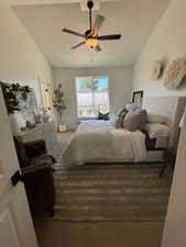 Carpeted bedroom with ceiling fan, vaulted ceiling, and a textured ceiling