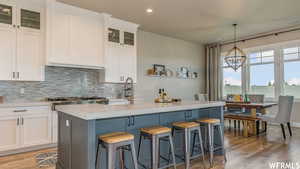 Kitchen featuring tasteful backsplash, wood-type flooring, white cabinets, and an island with sink