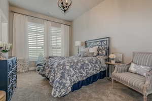 Bedroom featuring lofted ceiling, light colored carpet, and a chandelier