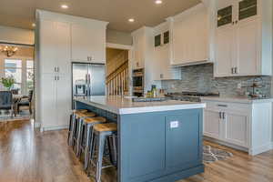 Kitchen with white cabinets, stainless steel appliances, light hardwood / wood-style floors, and a kitchen island with sink