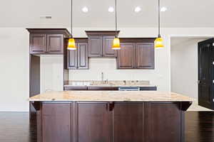 Kitchen with hanging light fixtures, sink, hardwood / wood-style flooring, and light stone counters