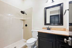 Bathroom featuring toilet, vanity, and a tile shower