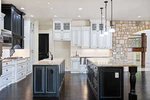 Kitchen with white cabinetry, stainless steel microwave, dark hardwood / wood-style flooring, and an island with sink