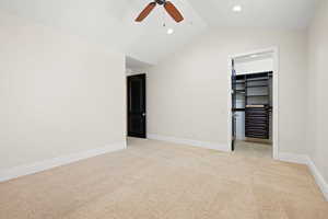 Unfurnished bedroom featuring light colored carpet, ceiling fan, vaulted ceiling, and a walk in closet