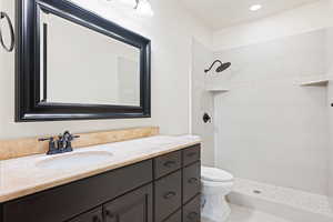 Bathroom with tiled shower, vanity, and toilet