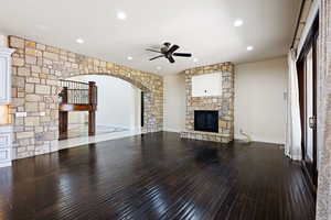 Unfurnished living room featuring a stone fireplace, ceiling fan, and wood-type flooring