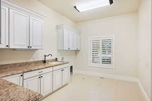 Laundry Room featuring sink, light tile patterned flooring, white cabinetry, and light stone countertops