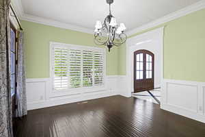 Living room adjacent to foyer featuring a notable chandelier, wood-type flooring, crown molding, and a healthy amount of sunlight