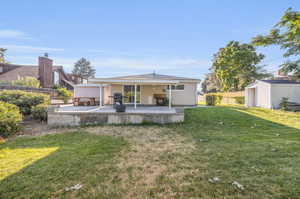 Back of property with a storage unit, a patio area, and a yard