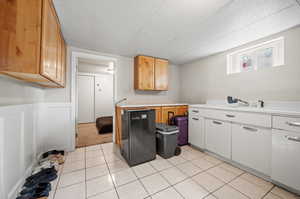 Kitchen with sink, light tile patterned flooring, fridge, and white cabinets