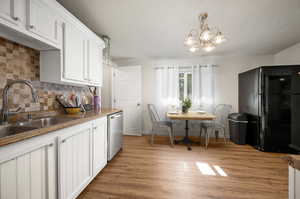 Kitchen featuring black refrigerator, dishwasher, tasteful backsplash, and light wood-type flooring