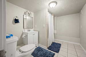 Full bathroom with vanity, shower / tub combo, toilet, a textured ceiling, and tile patterned flooring