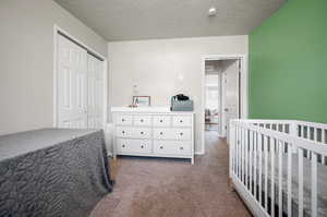 Carpeted bedroom featuring a nursery area, a closet, and a textured ceiling