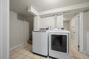 Laundry area with light tile patterned flooring, a textured ceiling, and washing machine and clothes dryer