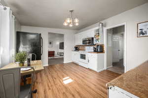 Kitchen with white cabinets, white range with electric stovetop, hanging light fixtures, black fridge, and light carpet