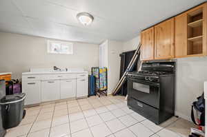 Kitchen with white cabinetry, light tile patterned flooring, black gas range, sink, and a paneled ceiling