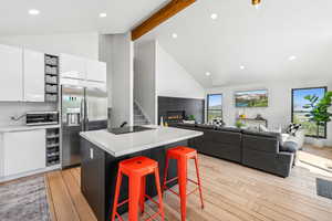 Kitchen with white cabinetry, stainless steel refrigerator with ice dispenser, light wood-type flooring, beamed ceiling, and a breakfast bar area