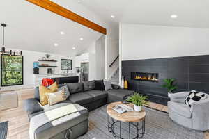 Living room featuring high vaulted ceiling, beamed ceiling, sink, light hardwood / wood-style floors, and a tiled fireplace