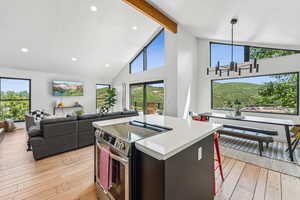 Kitchen with stove, hanging light fixtures, light wood-type flooring, beam ceiling, and a center island