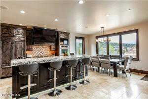 Kitchen with dark brown cabinets, light tile patterned floors, backsplash, hanging light fixtures, and a kitchen bar