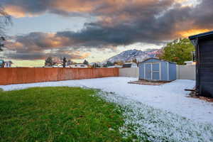 Yard layered in snow featuring a mountain view and a shed