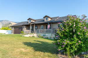 View of front of home with a mountain view, a porch, a garage, and a front lawn