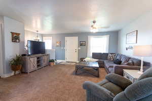 Living room featuring a textured ceiling, carpet flooring, a healthy amount of sunlight, and ceiling fan