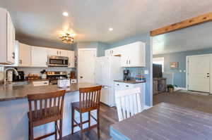 Kitchen featuring appliances with stainless steel finishes, white cabinets, sink, a kitchen breakfast bar, and dark colored carpet